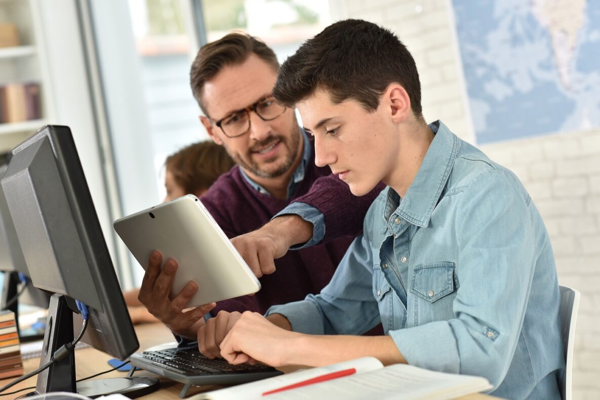 A man helping a student with their tablet and PC.