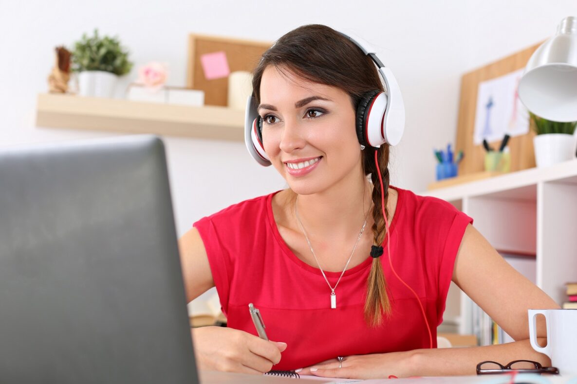 A smiling woman using a laptop with headphones.