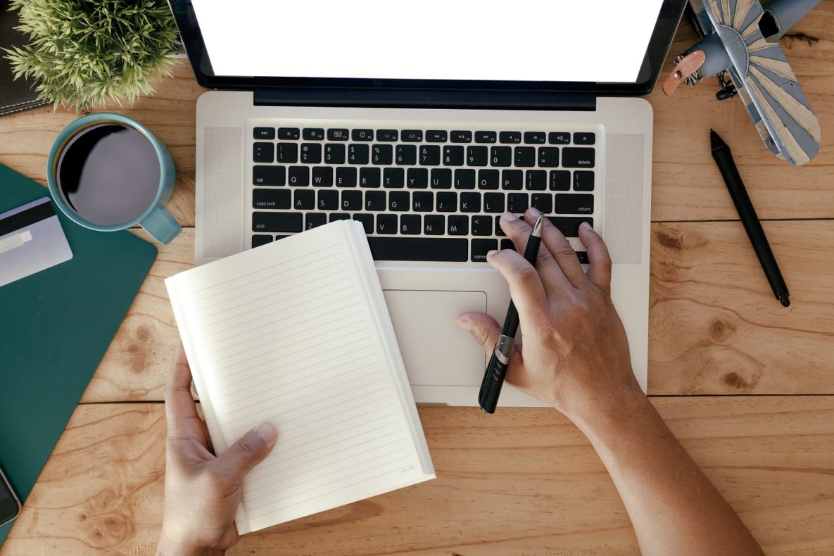 Fingers typing on a laptop with notepaper.