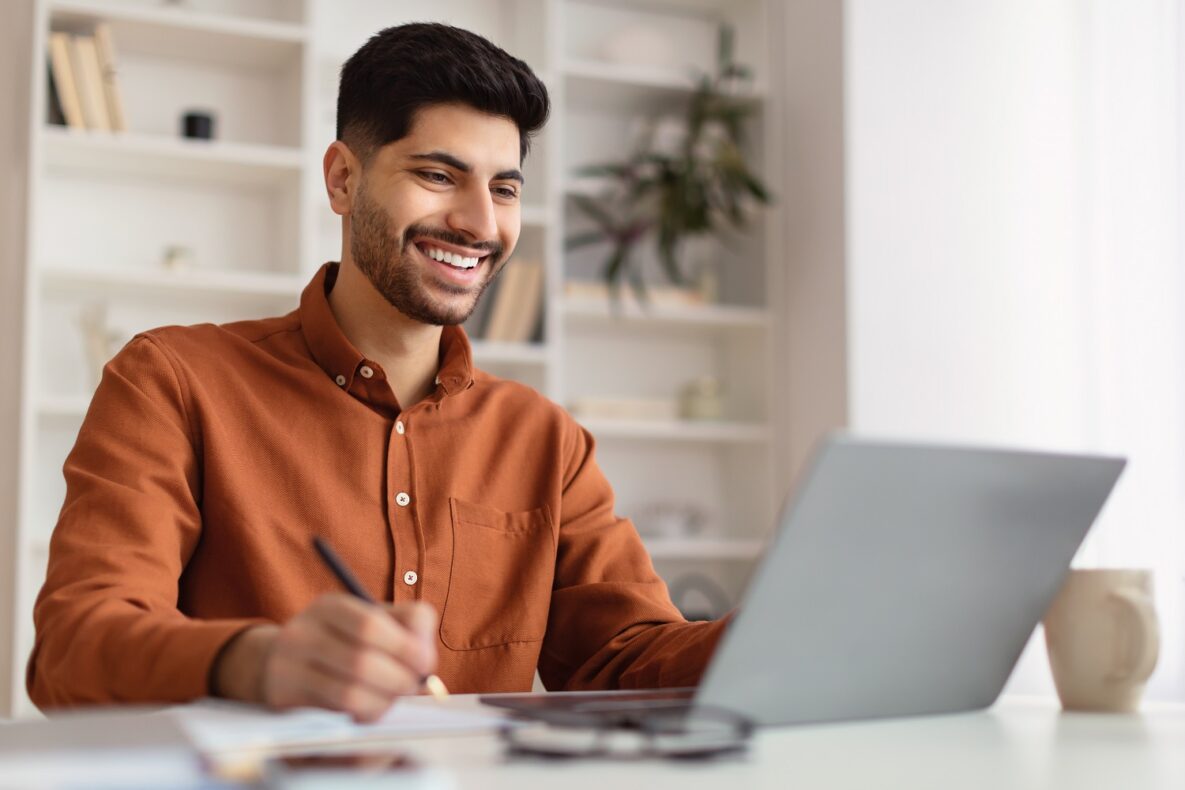 Portrait of a smiling man using his laptop and writing.