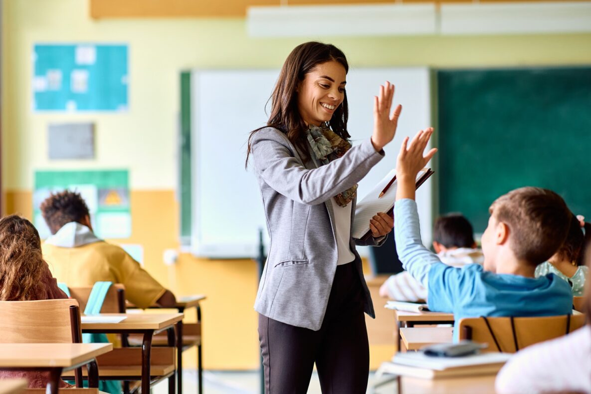 Happy elementary school teacher giving high-five to her student during class.