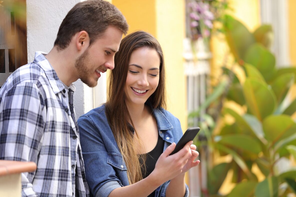 Happy couple checking content on their smart phone in the street.
