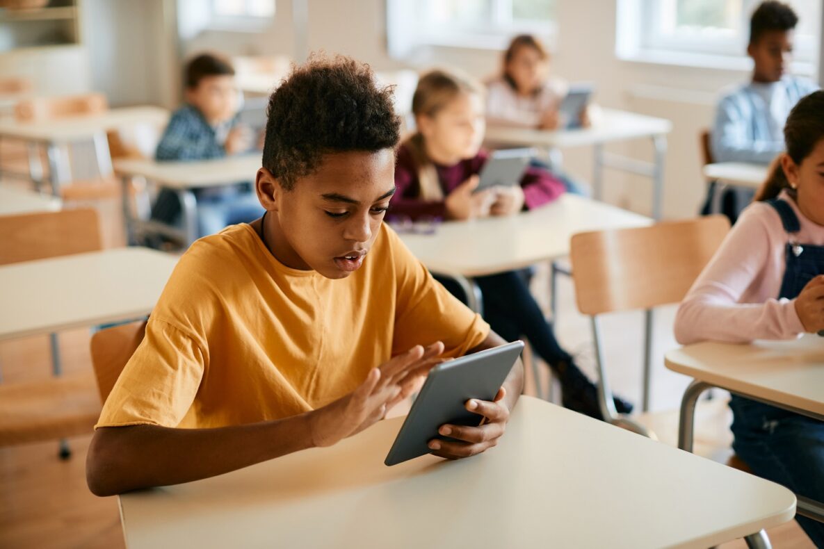 A young man in a classroom using his tablet.