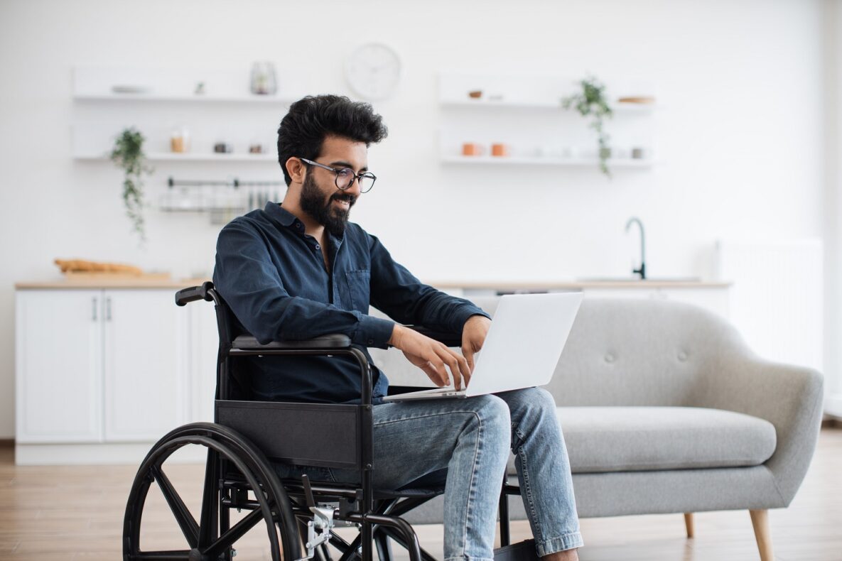 Man in wheelchair staying with laptop in open-plan kitchen.