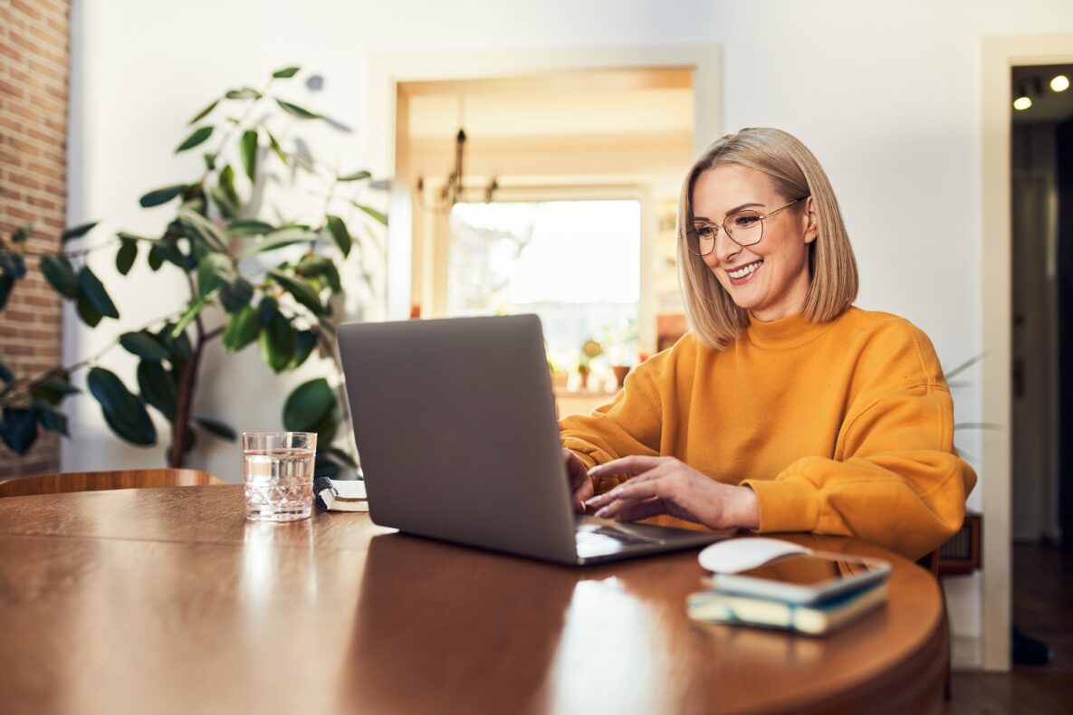 Happy mature woman using laptop while working remotely from home in living room.