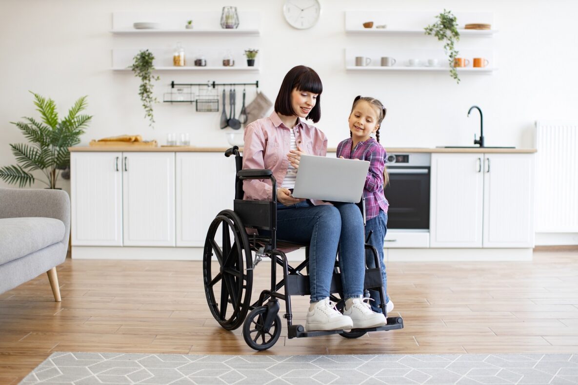 A woman in a wheelchair using her laptop with her young daughter.