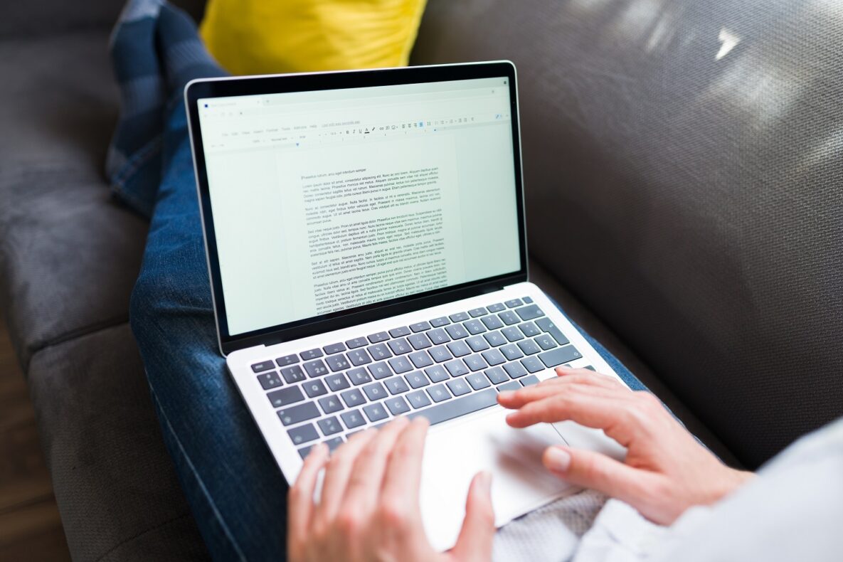 Adult man typing a letter or essay on the word processor in his laptop while resting on the couch.