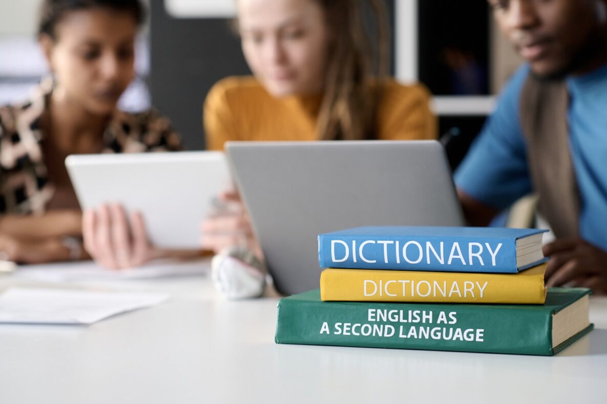 Close up background image of stacks of books on table with students studying in background