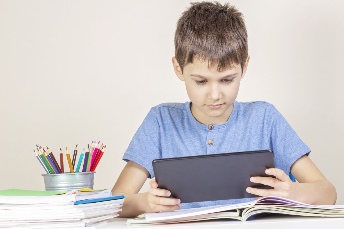 Kid with tablet computer sitting at table with books notebooks