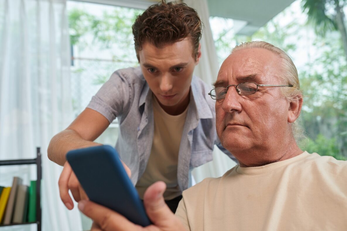 Young man helping grandfather with smartphone