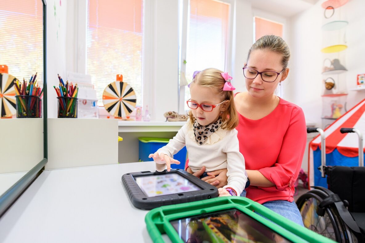 Non-verbal girl living with cerebral palsy, learning to use digital tablet device to communicate. People who have difficulty developing language or using speech use speech-generating devices.