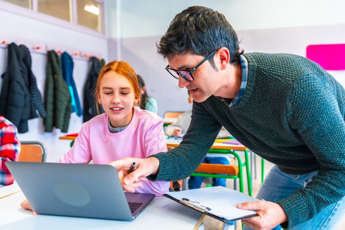 Teacher assisting a female student using a laptop during class