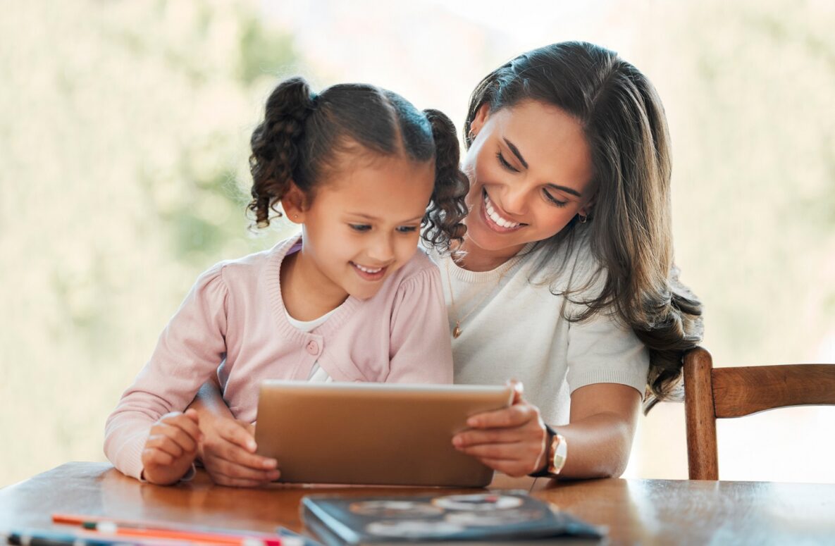 Smiling mother homeschooling her daughter with a digital tablet.